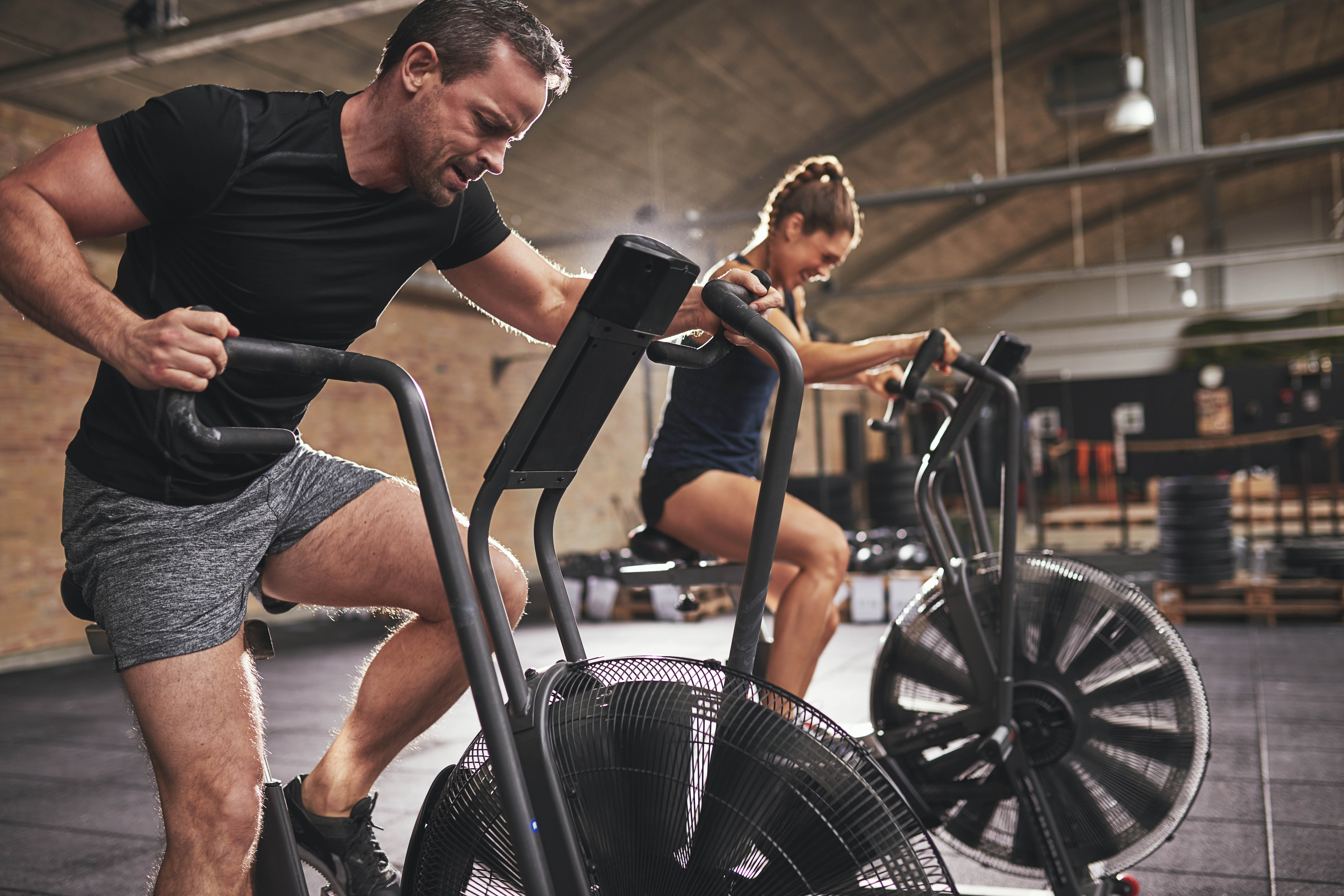 Fit man and woman on assault bikes mid-workout